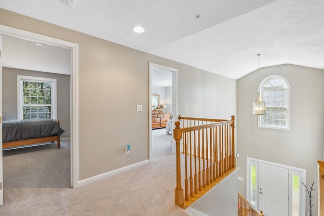 corridor with carpet flooring, baseboards, an upstairs landing, and vaulted ceiling