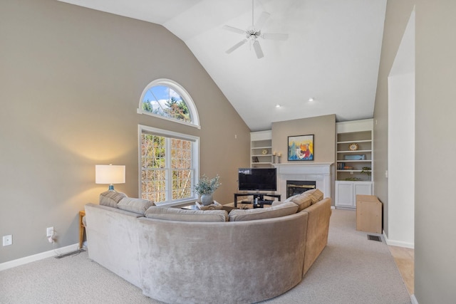 living area featuring a glass covered fireplace, baseboards, ceiling fan, and high vaulted ceiling