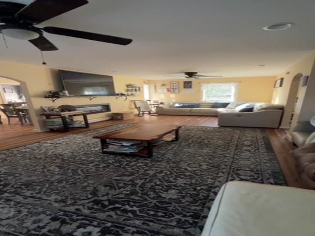 living area with arched walkways, ceiling fan, and wood finished floors