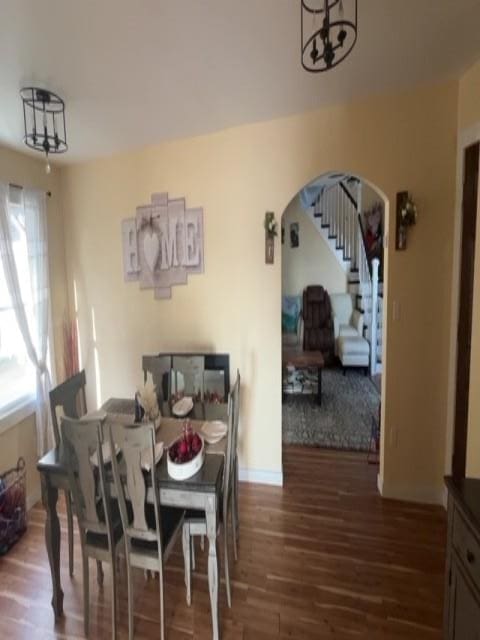 dining room with dark wood-style flooring, a notable chandelier, arched walkways, stairs, and baseboards
