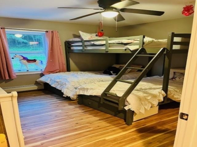 bedroom featuring a ceiling fan, a baseboard heating unit, and wood finished floors