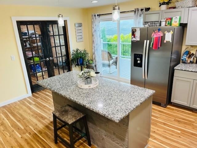 kitchen with a center island, hanging light fixtures, stainless steel fridge with ice dispenser, light stone counters, and light wood-style flooring