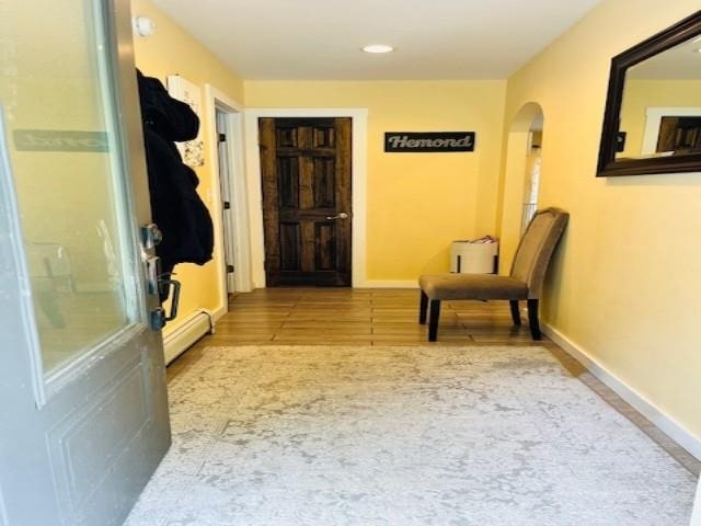 corridor featuring arched walkways, baseboards, a baseboard heating unit, and wood finished floors