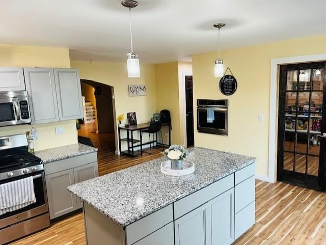 kitchen with appliances with stainless steel finishes, arched walkways, gray cabinetry, light stone counters, and light wood finished floors