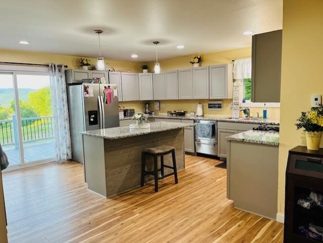 kitchen featuring light stone countertops, dishwasher, light wood-style flooring, a center island, and decorative light fixtures
