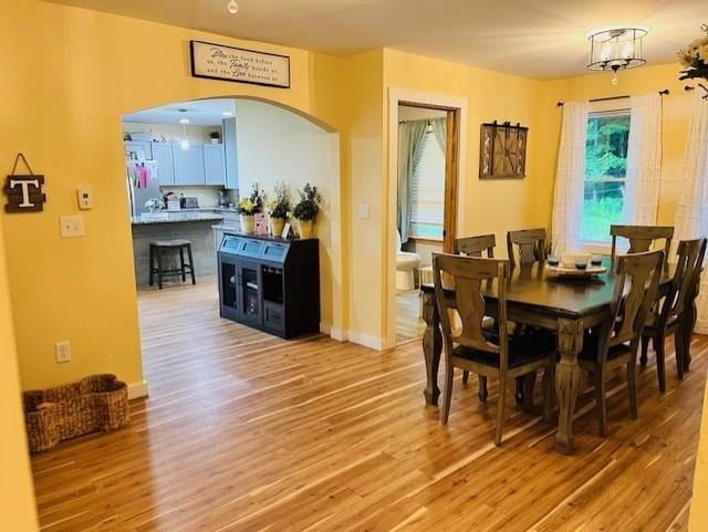 dining space with arched walkways and light wood-style floors