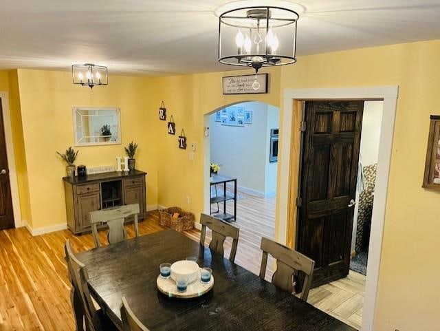 dining area featuring an inviting chandelier, arched walkways, light wood finished floors, and baseboards