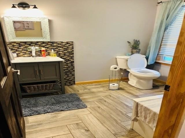 bathroom featuring toilet, baseboards, decorative backsplash, and vanity