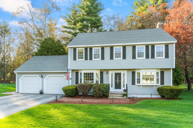 colonial inspired home featuring a front yard, a chimney, a shingled roof, concrete driveway, and an attached garage