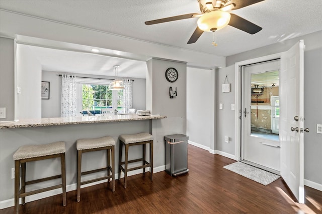 kitchen featuring baseboards, dark wood-style flooring, a kitchen breakfast bar, and light stone countertops