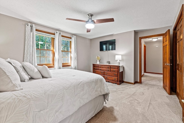 bedroom featuring ceiling fan, a textured ceiling, light colored carpet, and baseboards