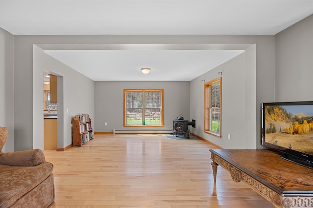 sitting room with a baseboard radiator, plenty of natural light, a wood stove, and light wood-type flooring