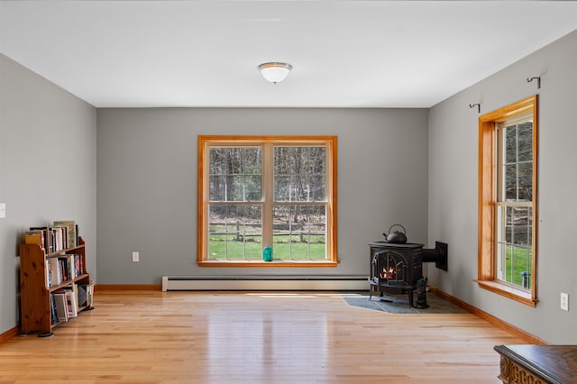 sitting room with baseboards, a wood stove, and light wood-style flooring