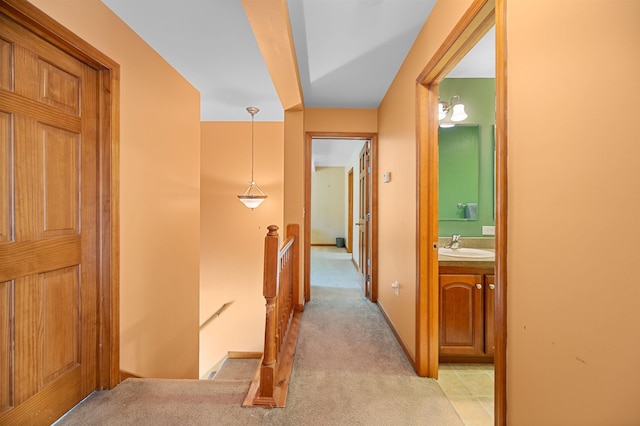 hall with a sink, light carpet, and an upstairs landing