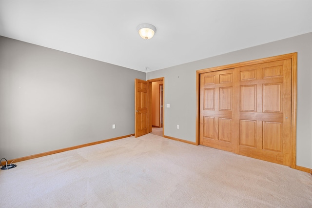 unfurnished bedroom featuring baseboards, light colored carpet, and a closet