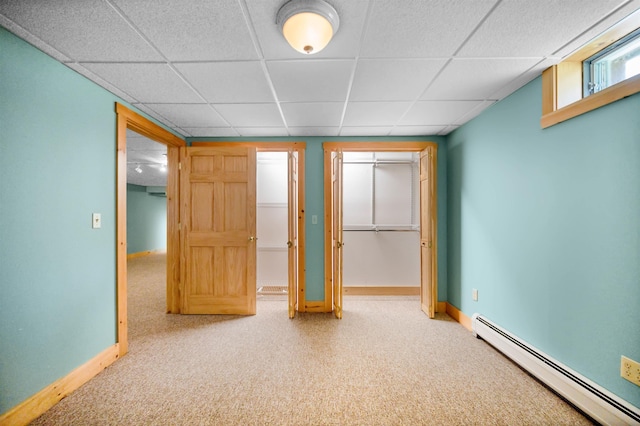 unfurnished bedroom featuring carpet flooring, baseboards, a baseboard heating unit, and a paneled ceiling