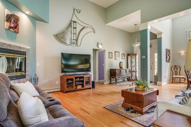 living area featuring a tiled fireplace, baseboard heating, wood finished floors, baseboards, and a high ceiling