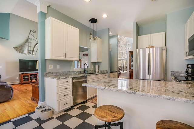 kitchen with a kitchen breakfast bar, appliances with stainless steel finishes, a sink, light floors, and white cabinetry