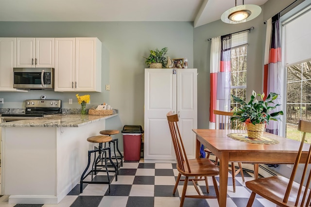 kitchen with appliances with stainless steel finishes, light stone counters, a breakfast bar area, tile patterned floors, and white cabinetry