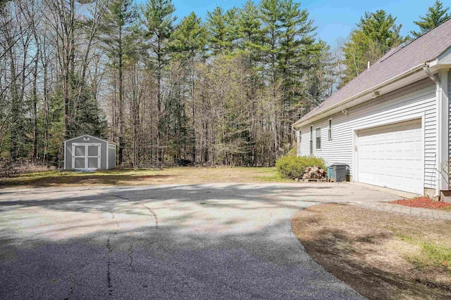exterior space featuring a forest view, a garage, an outdoor structure, a shed, and aphalt driveway