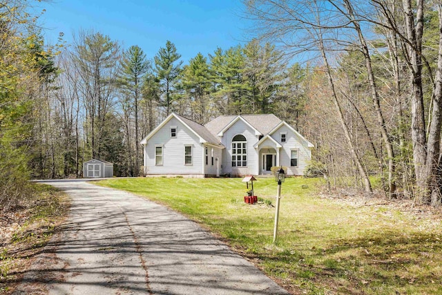 view of front of home with a front yard, a storage shed, a detached garage, an outdoor structure, and aphalt driveway
