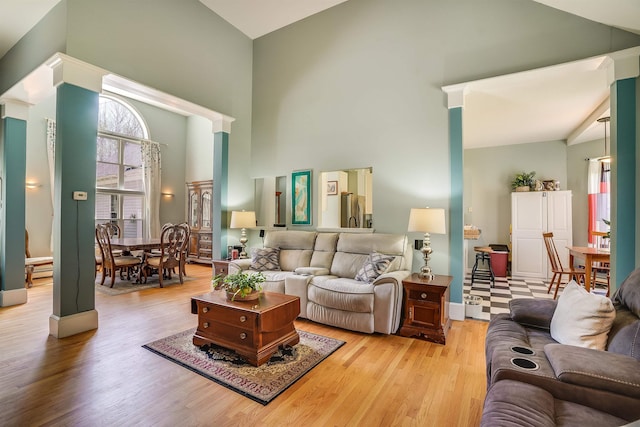 living area with baseboards, high vaulted ceiling, and light wood-style flooring