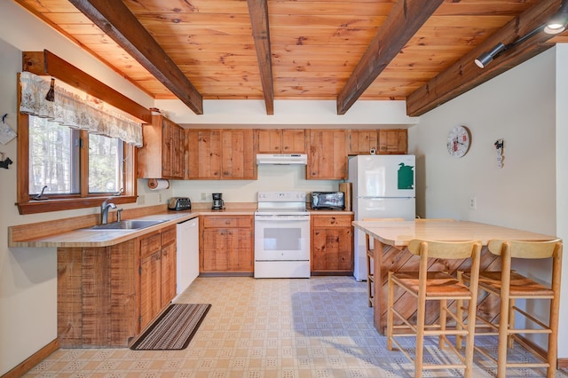 kitchen with white appliances, beamed ceiling, light floors, under cabinet range hood, and a sink