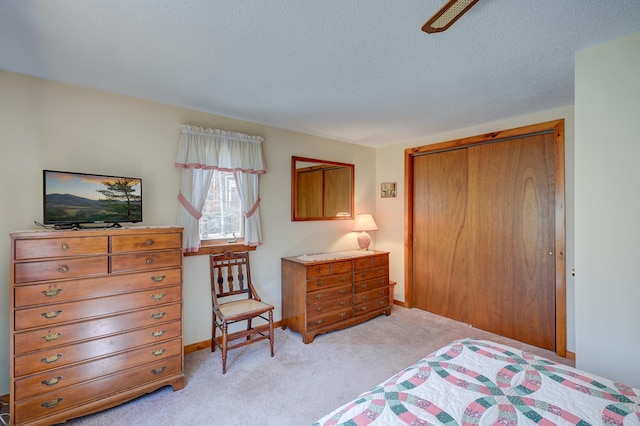 bedroom featuring a textured ceiling, light carpet, baseboards, and a closet