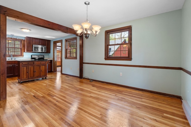 kitchen with an inviting chandelier, pendant lighting, baseboards, stainless steel microwave, and light wood-style floors