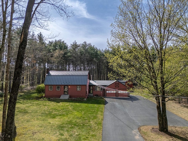 view of front facade with a front yard, a chimney, metal roof, an attached garage, and driveway