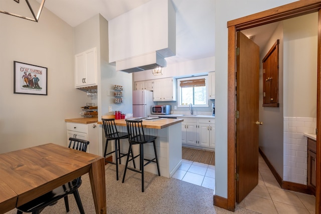 kitchen with a sink, white cabinetry, light tile patterned floors, and freestanding refrigerator