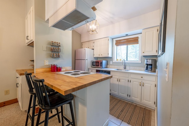 kitchen featuring freestanding refrigerator, butcher block counters, a peninsula, a sink, and exhaust hood
