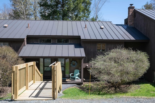 back of house featuring a standing seam roof, a chimney, and metal roof
