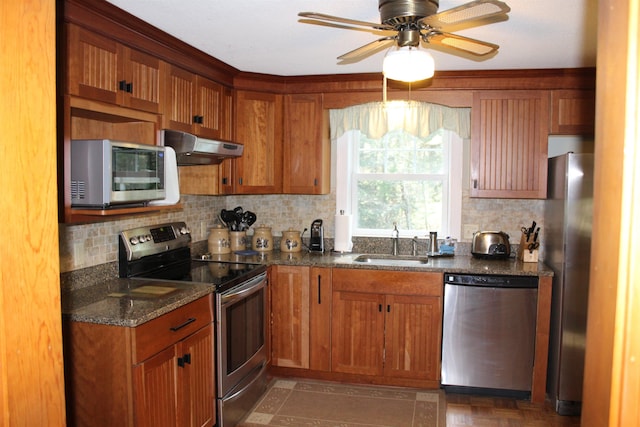 kitchen with backsplash, a sink, dark stone countertops, under cabinet range hood, and stainless steel appliances