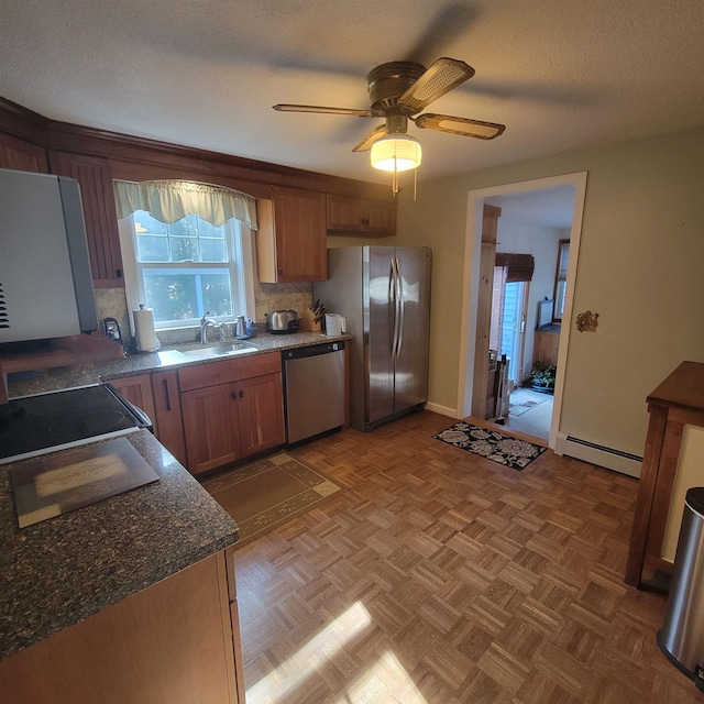 kitchen with ceiling fan, decorative backsplash, appliances with stainless steel finishes, a sink, and a baseboard heating unit