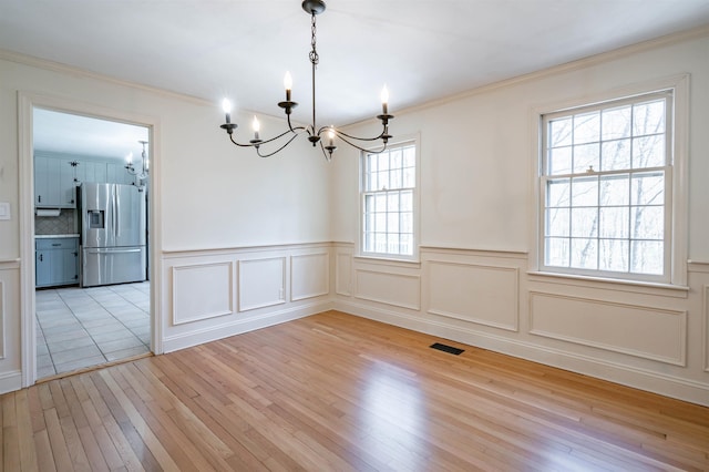 unfurnished dining area with crown molding, wainscoting, light wood-style flooring, and a notable chandelier