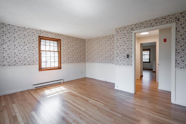 spare room featuring light wood-style floors, wainscoting, a baseboard heating unit, and wallpapered walls
