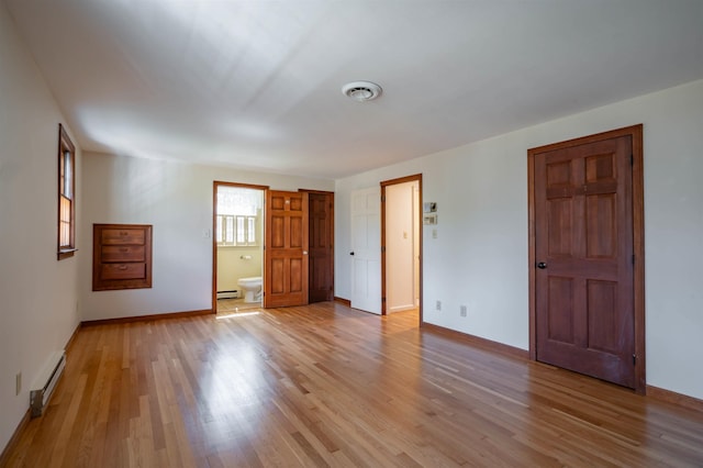 unfurnished bedroom featuring baseboards, baseboard heating, light wood-type flooring, and visible vents
