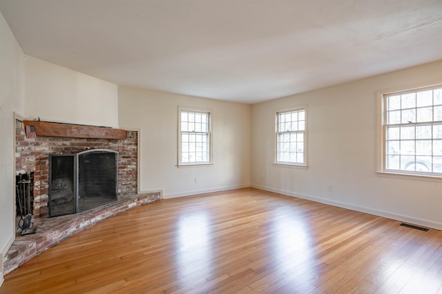 unfurnished living room with baseboards, a brick fireplace, wood finished floors, and visible vents