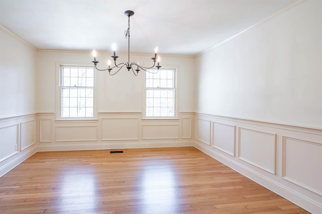 unfurnished dining area with wainscoting, a notable chandelier, light wood-style floors, ornamental molding, and a decorative wall