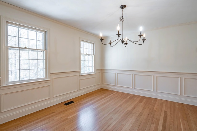 unfurnished room with visible vents, a wainscoted wall, light wood finished floors, a notable chandelier, and ornamental molding