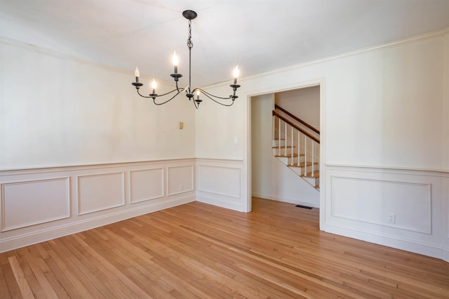 unfurnished dining area featuring a chandelier, ornamental molding, stairway, and a decorative wall
