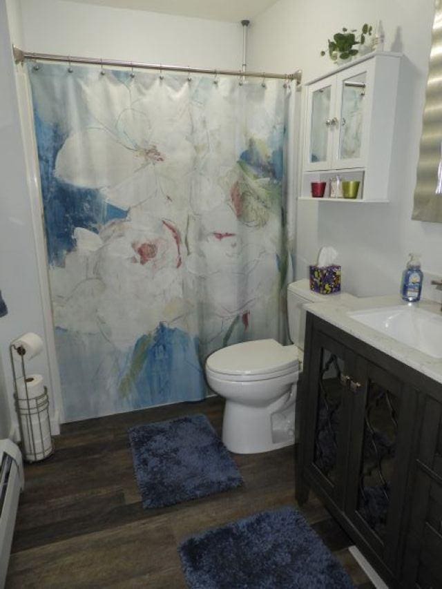bathroom featuring vanity, toilet, curtained shower, wood finished floors, and a baseboard heating unit