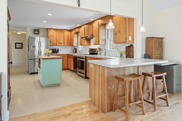 kitchen with a peninsula, under cabinet range hood, tasteful backsplash, light wood-style flooring, and appliances with stainless steel finishes
