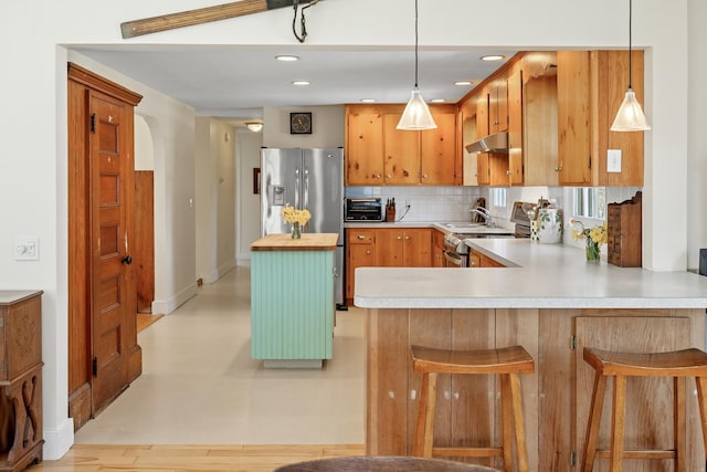 kitchen with tasteful backsplash, stainless steel appliances, a peninsula, a toaster, and under cabinet range hood