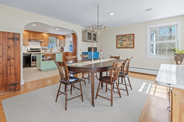 dining space with arched walkways, light wood-style flooring, a baseboard heating unit, and a healthy amount of sunlight
