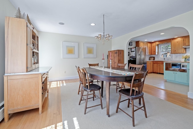 dining area featuring light wood-style floors, arched walkways, recessed lighting, and a notable chandelier