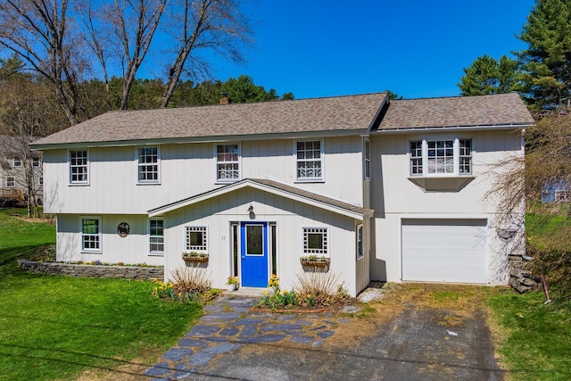 view of front of house with an attached garage, aphalt driveway, roof with shingles, and a front yard
