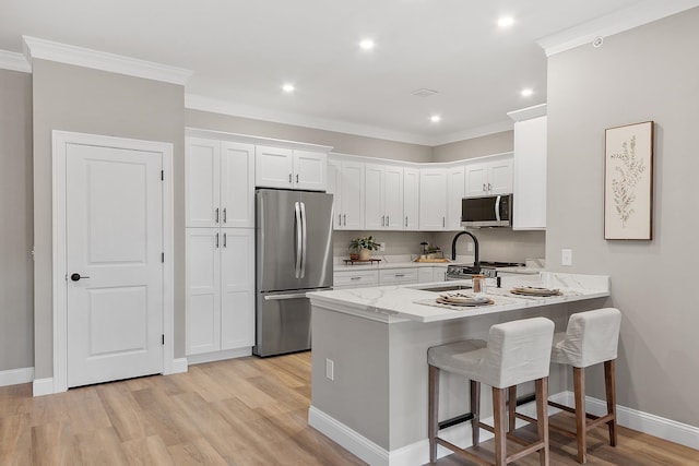 kitchen with a sink, light wood finished floors, stainless steel appliances, white cabinetry, and a peninsula