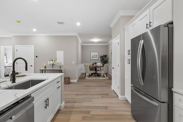 kitchen with ornamental molding, white cabinets, a sink, light wood finished floors, and appliances with stainless steel finishes